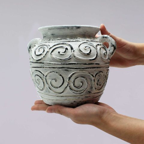 A cream greek clay plant pot with black swirling patterns and handles held in hands perfect for plants