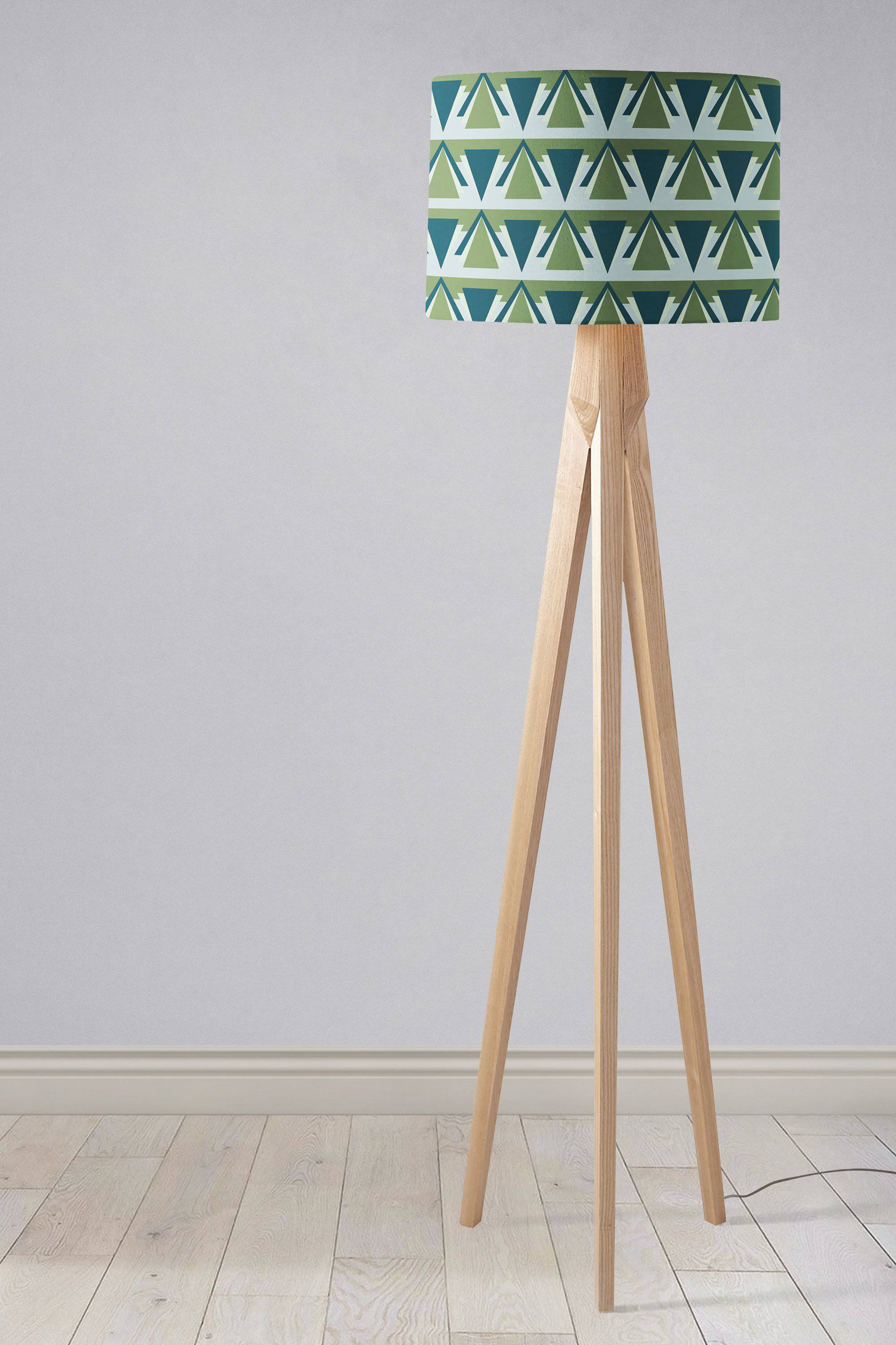 A modern table lamp with a green and grey art deco lampshade and three slender wooden legs in tripod style