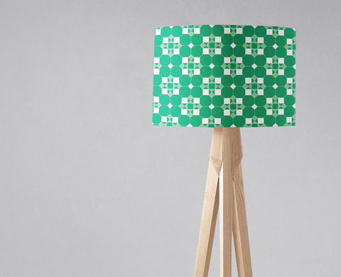 A modern table lamp with a bold green and white geometric design lampshade on light wood tripod legs