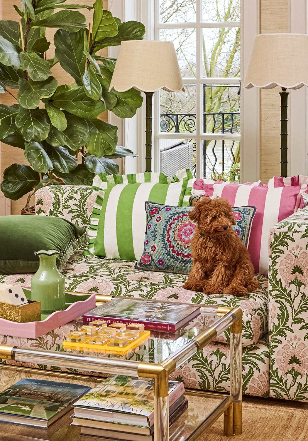 A fluffy brown poodle sits on a patterned sofa with green cabana stripe ruffled cushion cover and colorful pillows