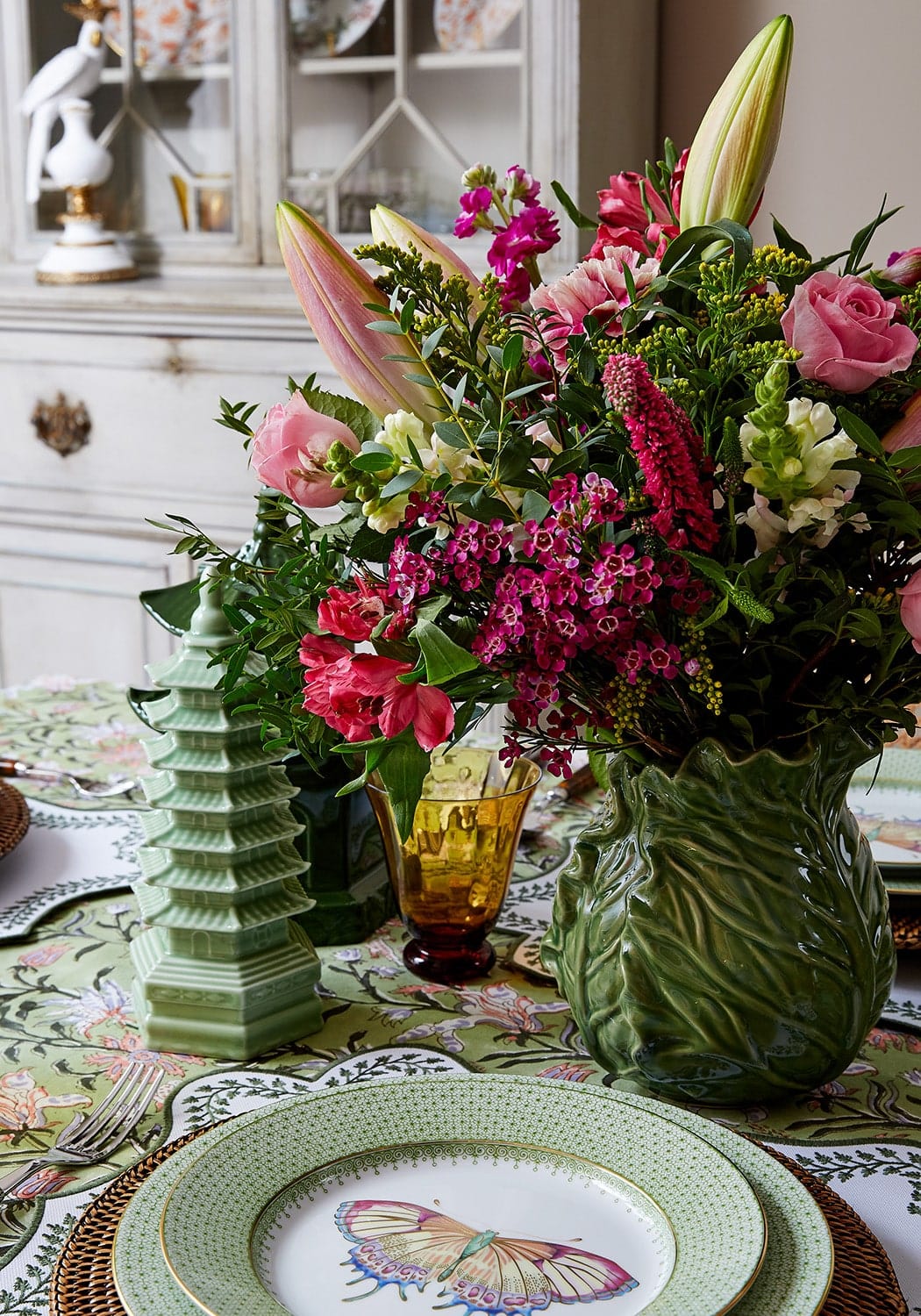 A lush floral print tablecloth paired with a vibrant arrangement in a textured green ceramic vase with leaf ridges