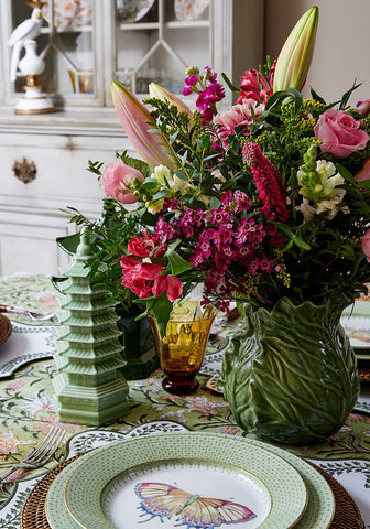 A lush floral print tablecloth paired with a vibrant arrangement in a textured green ceramic vase with leaf ridges