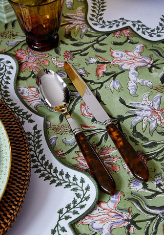 A pair of elegant cutlery with tortoiseshell handles on a green with envy floral print tablecloth