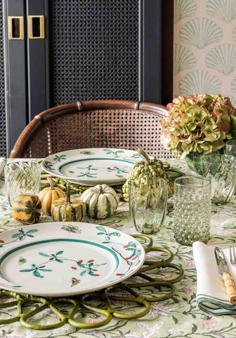 White ceramic plate with green and red botanical print on woven placemat on green with envy floral print tablecloth