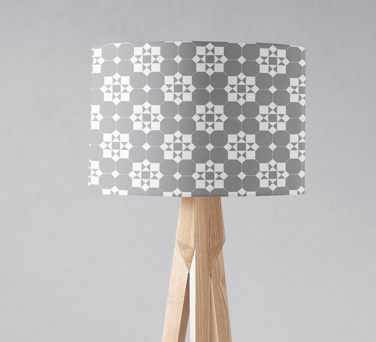 A modern table lamp with a geometric lampshade in gray and white tiles design on a light wood tripod base