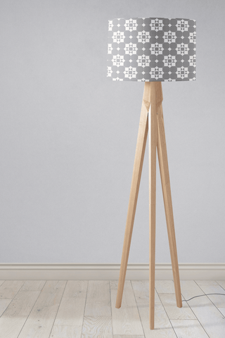 A modern table lamp with a gray and white geometric lampshade featuring tiles design and slim wooden tripod legs