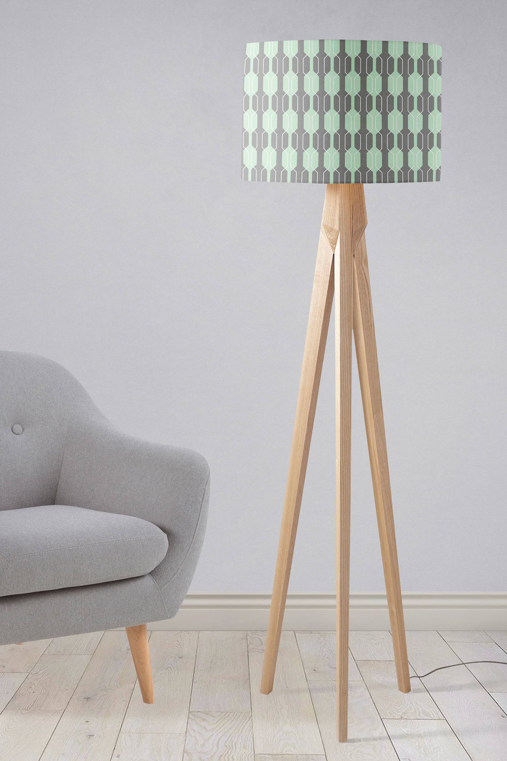 A table lamp with a mint green and gray geometric lampshade and a wooden tripod lamp base