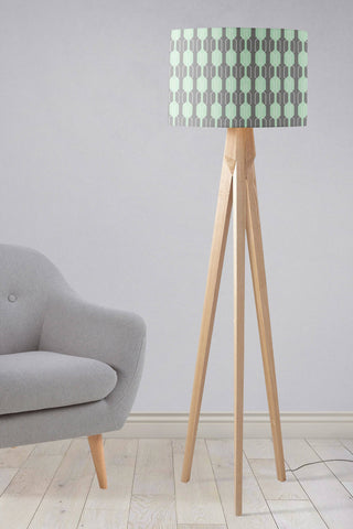 A table lamp with a mint green and gray geometric lampshade and wooden tripod lamp base