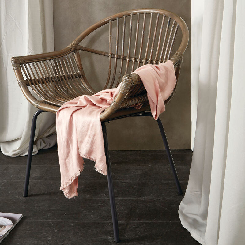 A grey wash natural rattan chair with curved back and black metal legs draped with a soft pink scarf