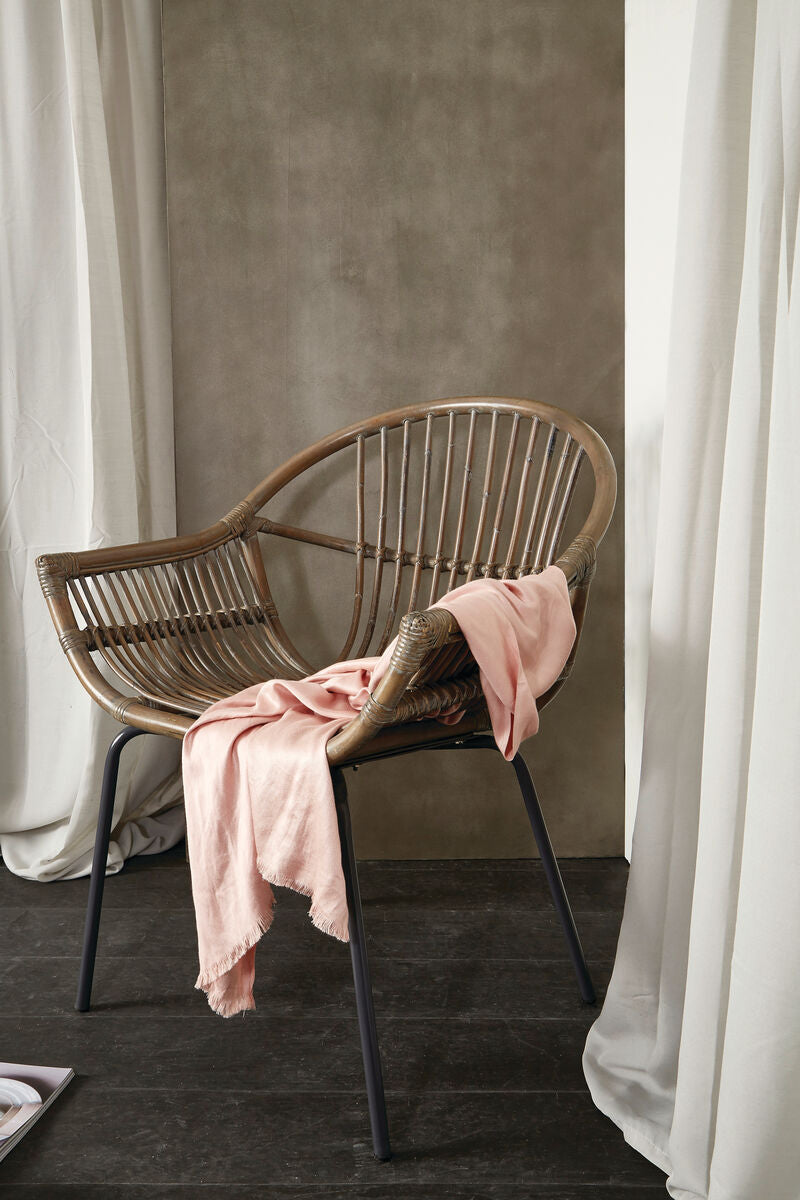 Grey wash natural rattan chair with curved back and black metal legs draped with soft pink fabric
