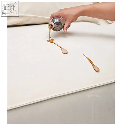 A hand pours dark liquid on cream velvet fabric of the grimm three seater sofa showing stain resistance on this three seater sofa