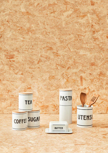 White metal tea canister and white ceramic kitchen canisters with black lettering for tea coffee sugar pasta and utensils