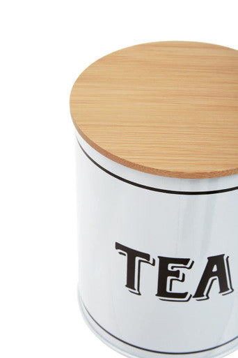White metal tea canister grocer with a cylindrical design, light wood lid, and black tea lettering