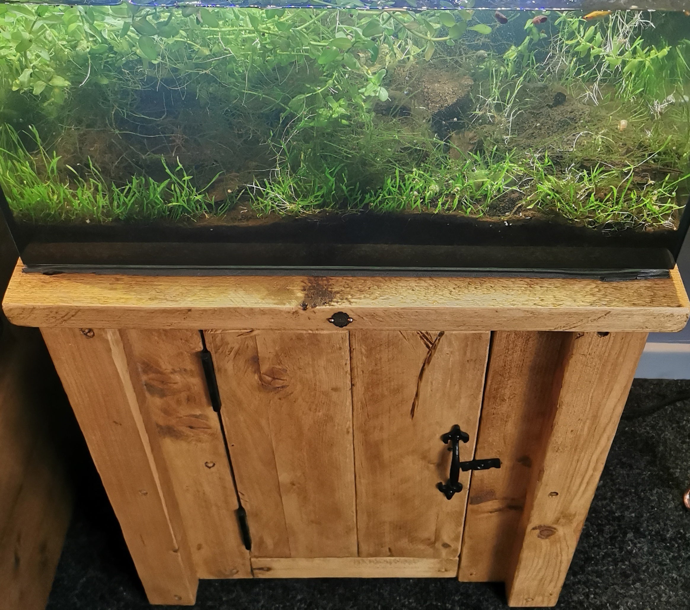 A rustic wooden fish tank aquarium stand with natural finish black metal hinges and handles handmade custom sizes and colours