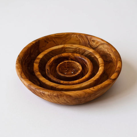Set of four handmade olive wood bowls with silky polished interior and warm golden-brown swirling natural grain patterns