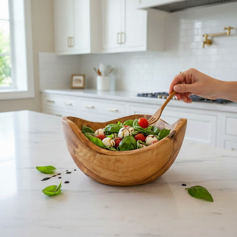 A rustic light brown olive wood salad bowl with smooth handcrafted finish and unique natural bark edge holding fresh greens and cherry tomatoes