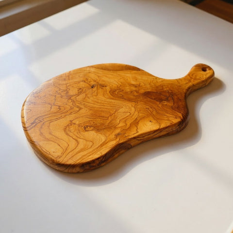 Handmade round freeform olive wood cutting board with smooth natural finish and bold swirling grain patterns