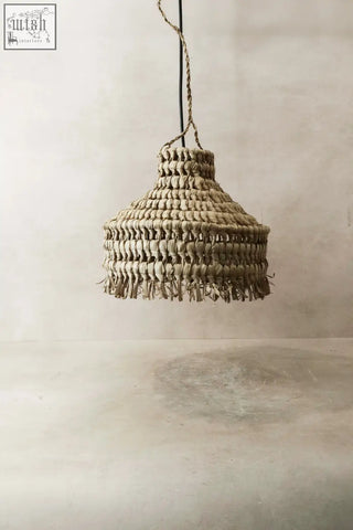 Beige handmade ilala palm lamp shade with woven rattan and fringed edge hanging by black cord suspension