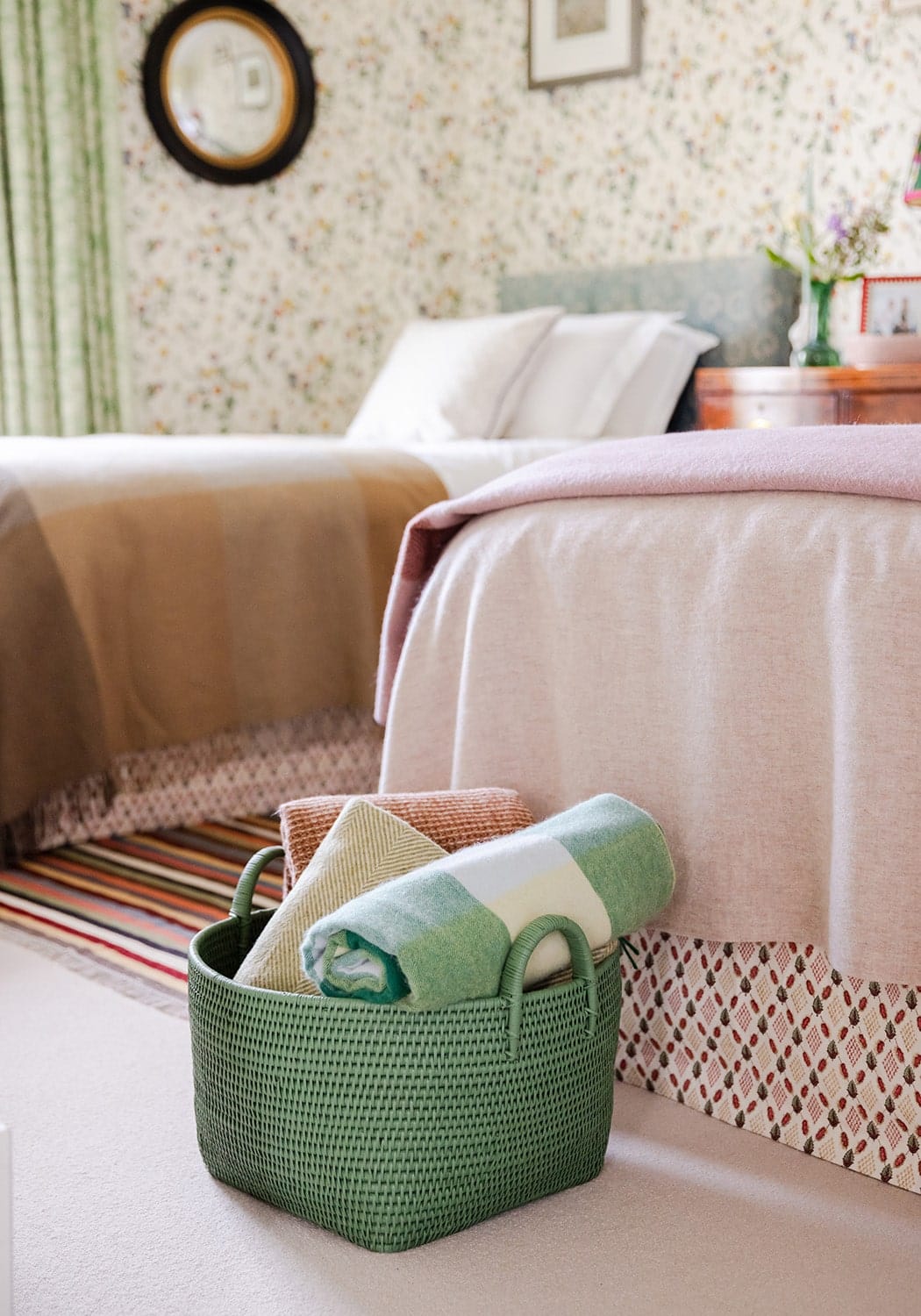 Green handwoven rattan basket with two handles holding rolled towels in earthy tones for storage or decor