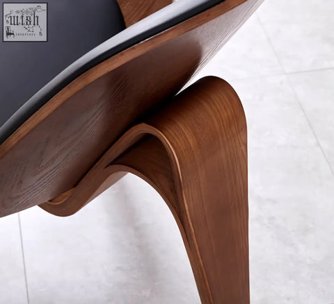 Curved walnut wood leg of hans wegner ch07 shell chair with sleek black upholstered seat visible from the back side