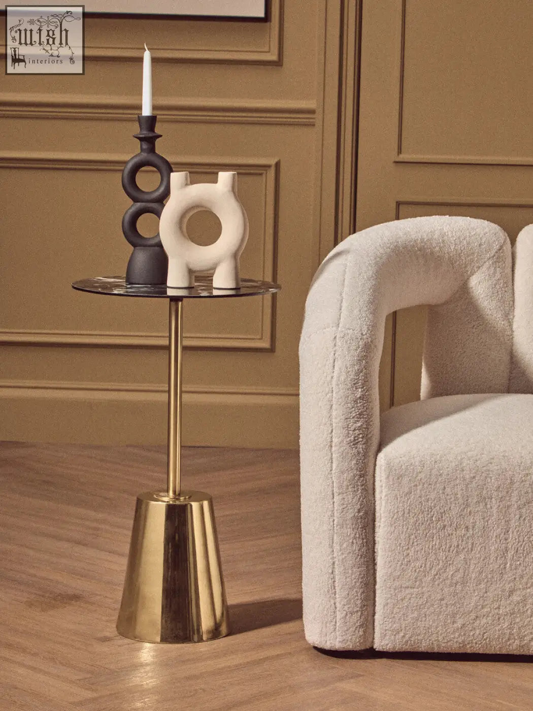 Gold toned cylindrical side table with reflective glass top and flared base next to a large black candle holder