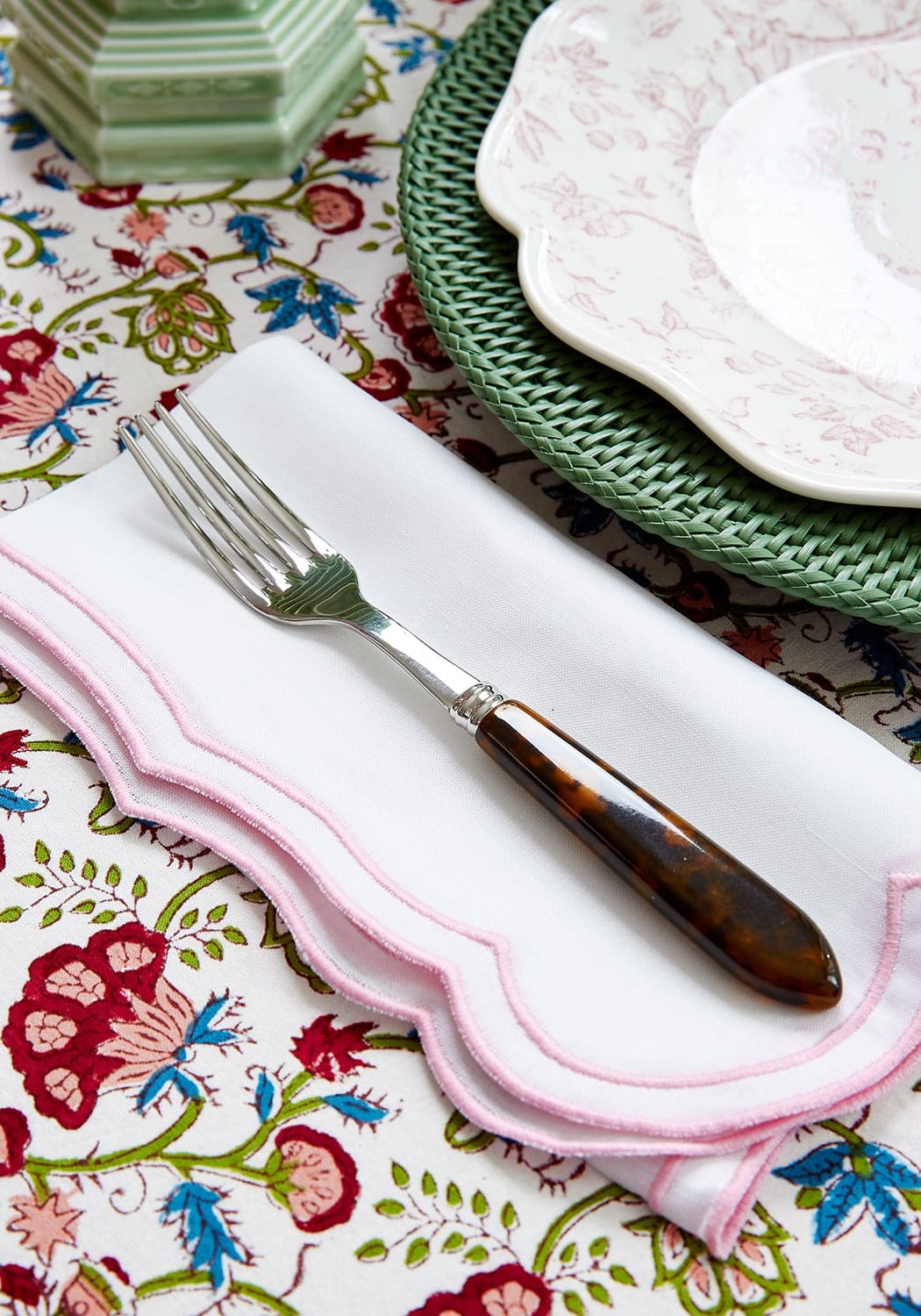 A silver fork with tortoiseshell handle resting on a white napkin next to a green harbour island round rattan charger set of 4