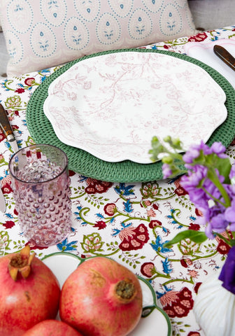 White ceramic plate with pink floral patterns and scalloped edge on a green woven harbour island rattan charger set of 4
