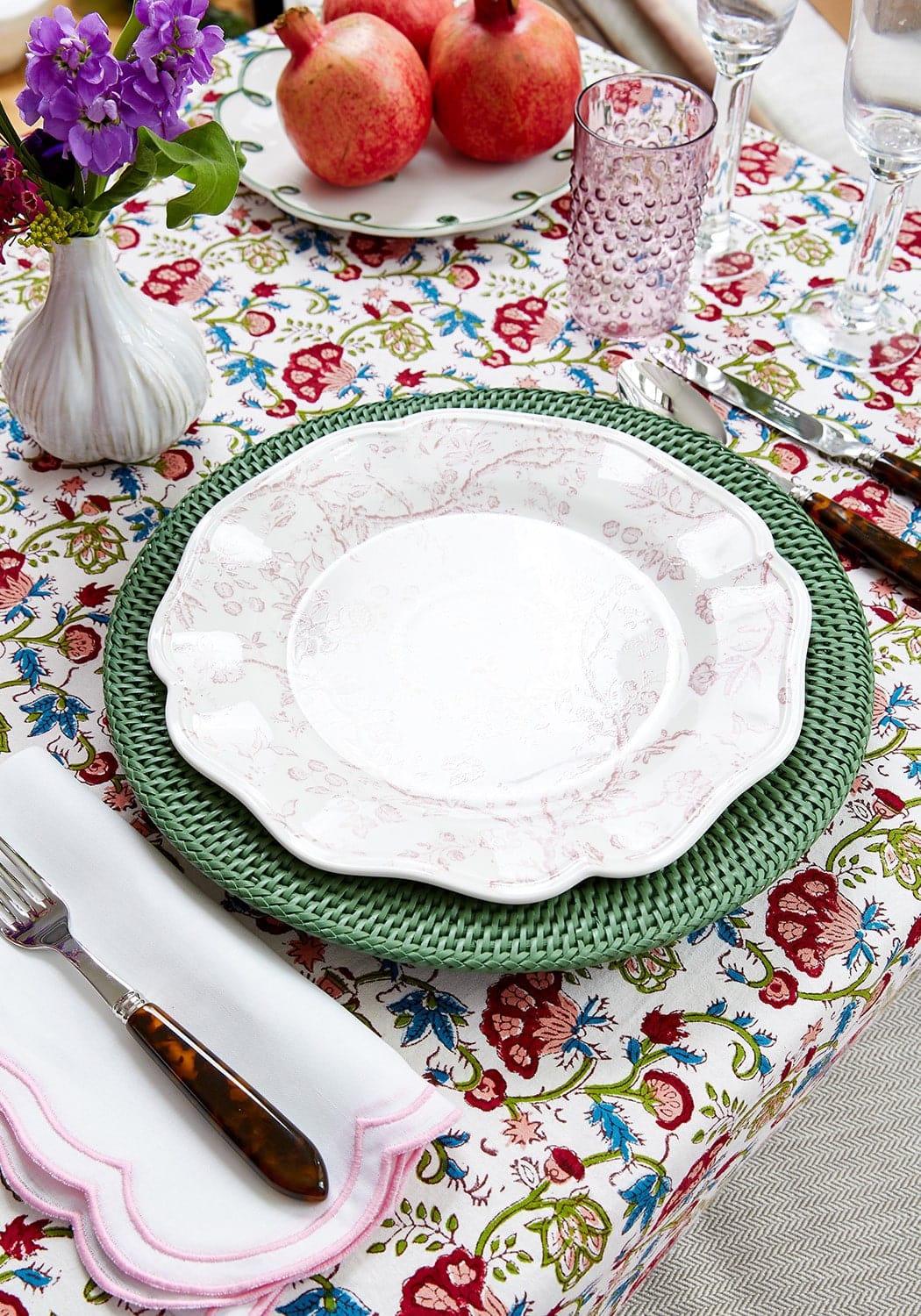White ceramic plate with floral pattern on scalloped edges resting on green harbour island round rattan charger set of 4