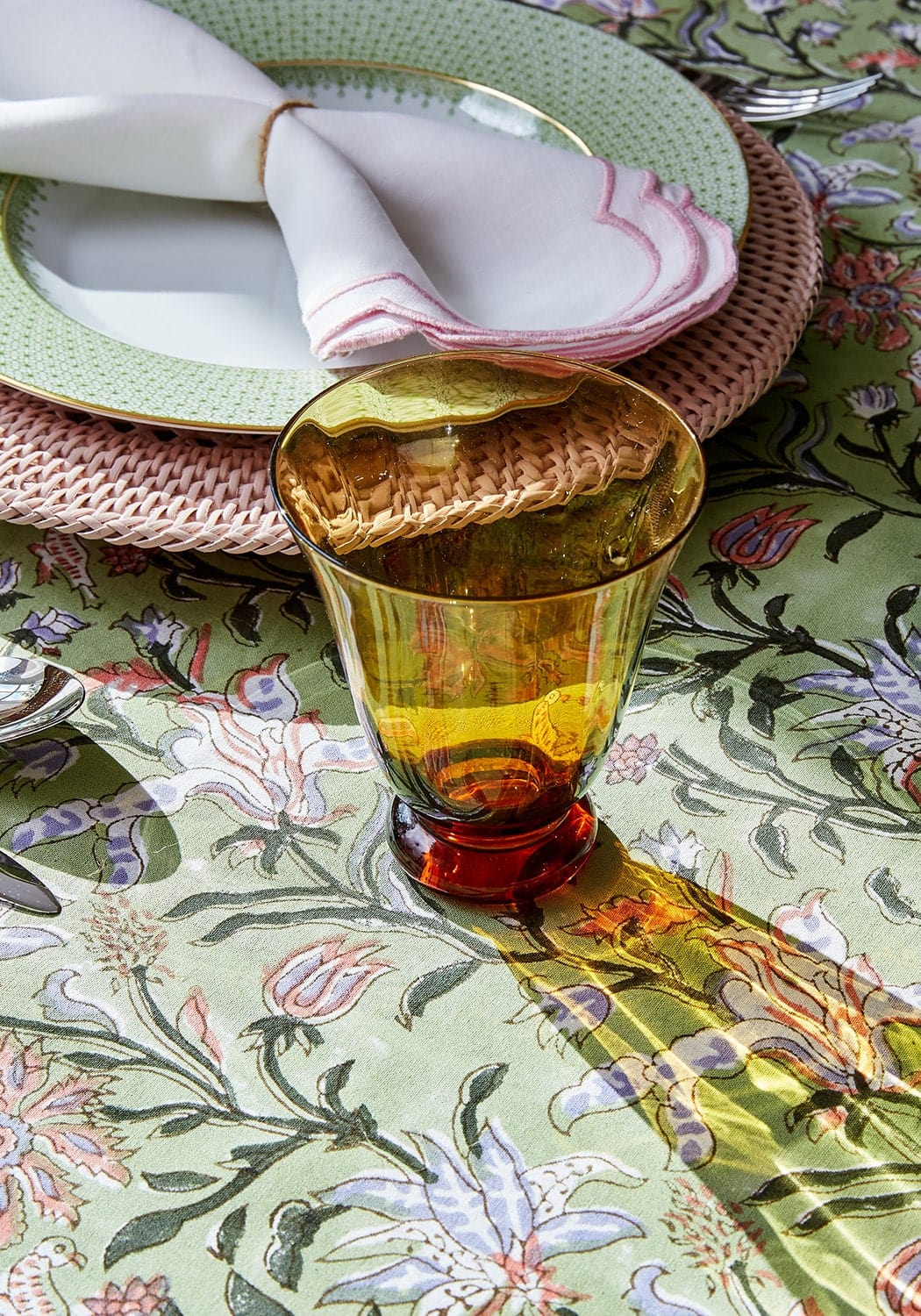 Amber tinted glass tumbler with red base and scalloped rim placed on pink harbour island round rattan charger placemat set