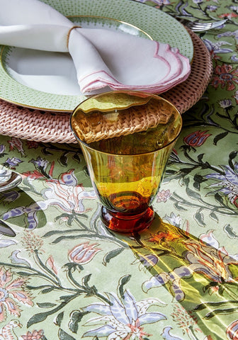 Amber tinted glass tumbler with red base and scalloped rim placed on pink harbour island round rattan charger placemat set