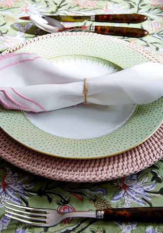 A white napkin with pink embroidery tied with rustic twine on a harbour island round rattan charger placemat pink set of 4