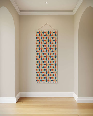 A rectangular harlequin pattern tapestry with orange blue and beige diamonds on a cream background wall hanging