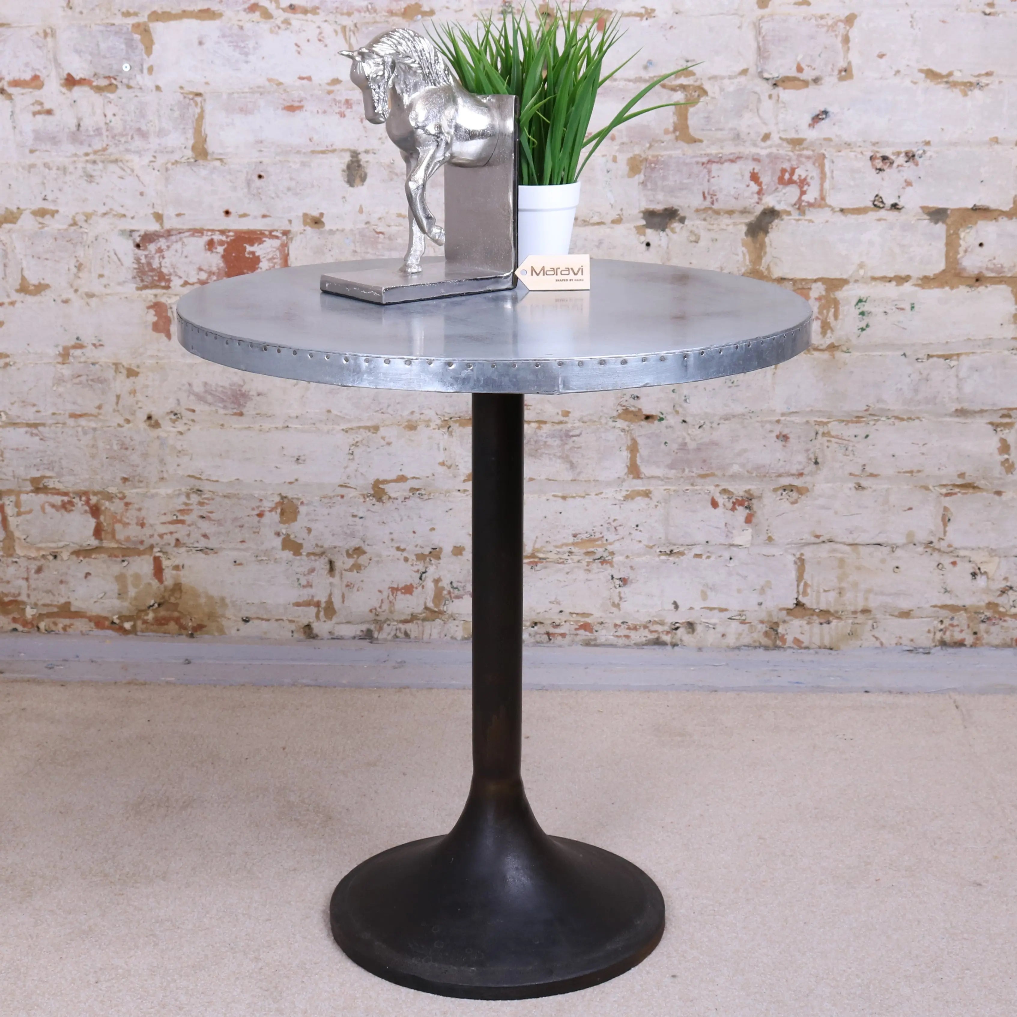 Hatra industrial style round side table with silver metal riveted top and dark matte pedestal base in industrial style