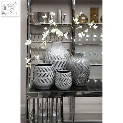 Set of three grey ceramic silver small planters with geometric cut-out patterns on a mirrored shelf