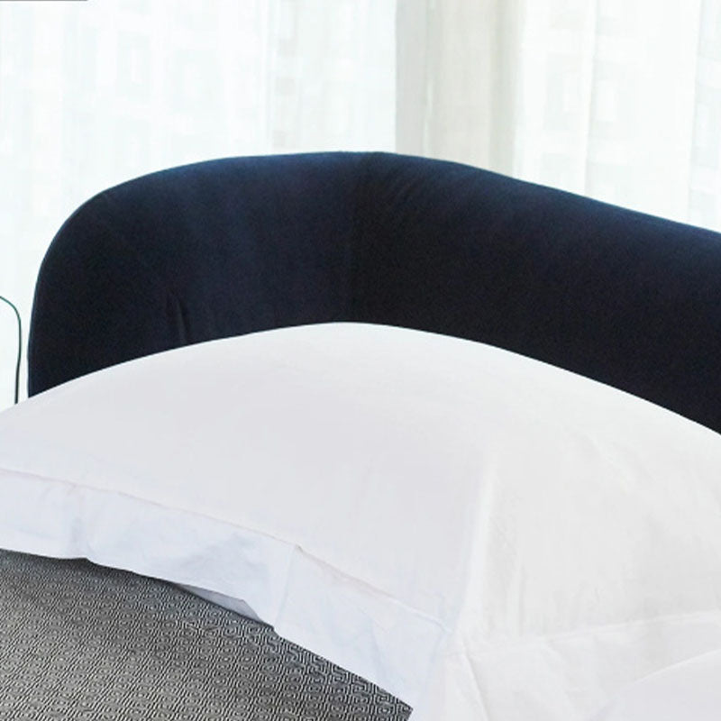 White pillow with a clean finish resting against a plush navy blue velvet headboard on the heloise king size bed