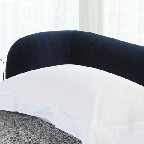 White pillow with a clean finish resting against a plush navy blue velvet headboard on the heloise king size bed