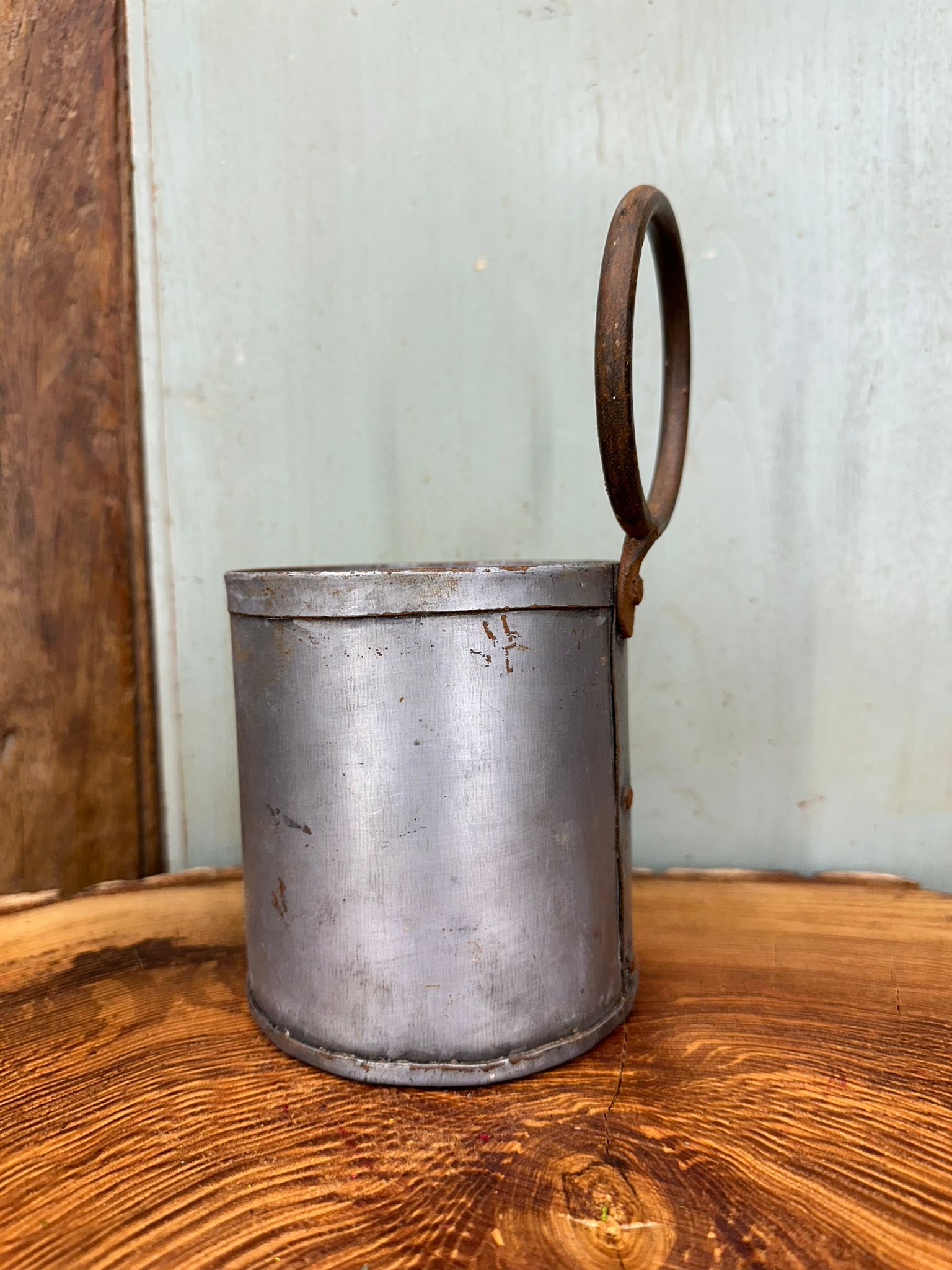 A weathered cylindrical metal herb plant pot with a rusted circular handle for desk tidy or cutlery holder use
