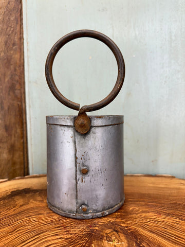 A rustic cylindrical metal herb plant pot with weathered silver finish and dark brown rusted handle for desk tidy