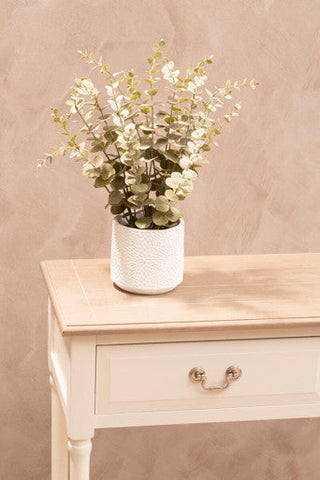 A white textured ceramic vase with artificial eucalyptus sits on a heritage white rectangular console table with drawers