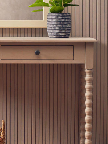 A blue and white striped ceramic planter with a ribbed texture on a heritage two drawer desk with natural wash