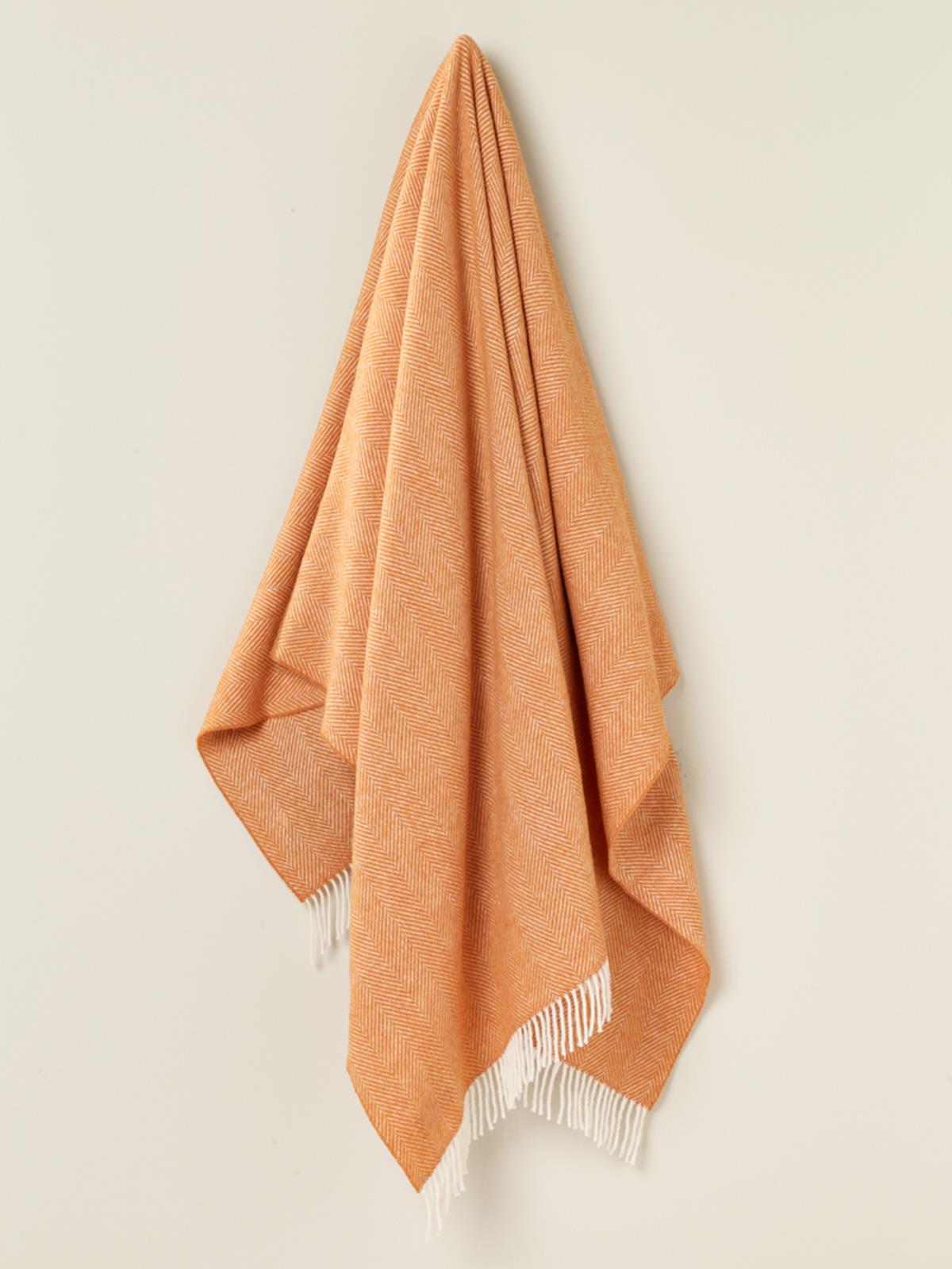 A soft peach-colored herringbone merino lambswool throw with white fringe perfect for cozying up