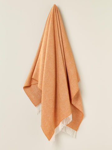 A soft peach-colored herringbone merino lambswool throw with white fringe perfect for cozying up
