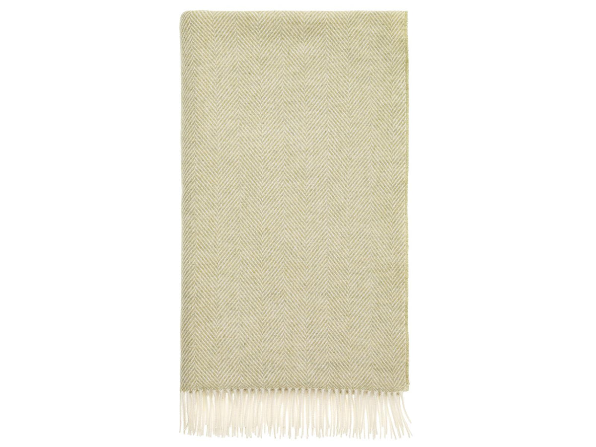 A soft sage herringbone merino lambswool throw with delicate white fringe perfect for cozying up