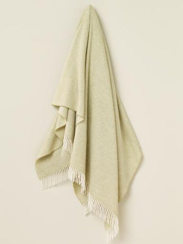 A soft sage herringbone merino lambswool throw with delicate white fringe perfect for cozying up