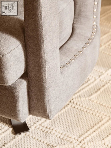 Beige hestia ash velvet swivel chair with tufted upholstery and silver nailhead trim along the edges