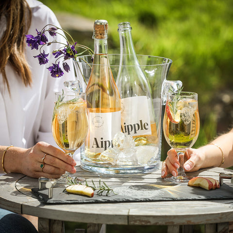 A clear glass ice bucket holding two bottles of sparkling apple cider with highland cow craft beer glasses set of 2