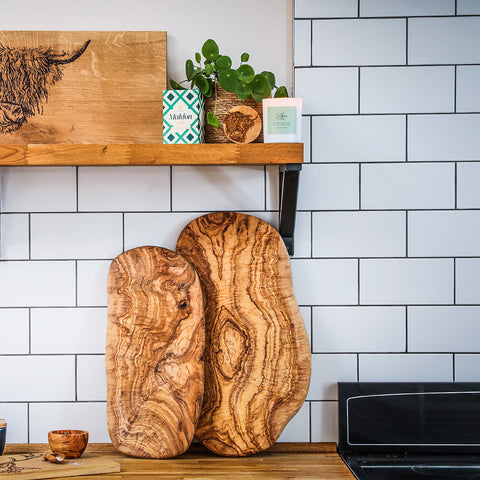 Two rustic olive wood cutting boards with warm brown tones paired with highland cow fresh fennel soy wax candle