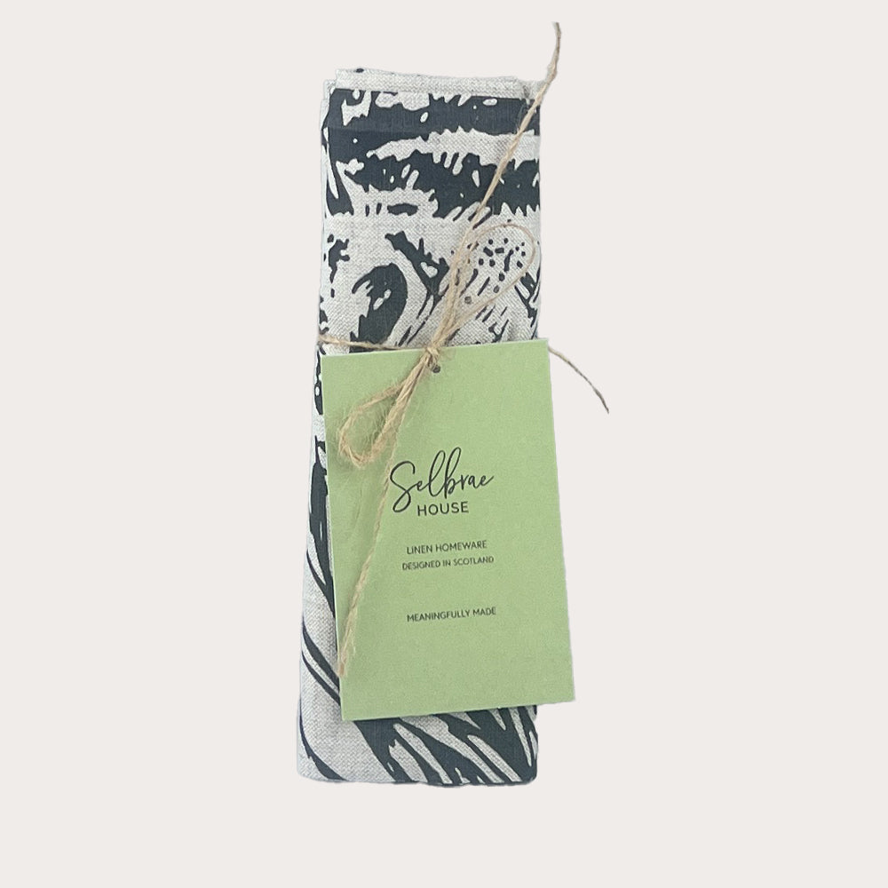 A rolled-up black and white abstract pattern linen tea towel from selbrae house tied with twine labeled linen homeware designed in scotland