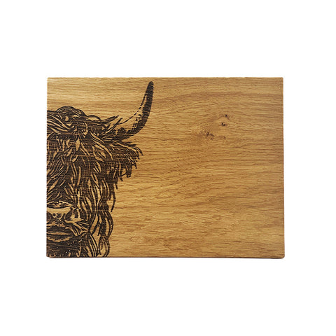 A rustic oak bar board with a detailed black burned illustration of a highland cow’s head on the left side