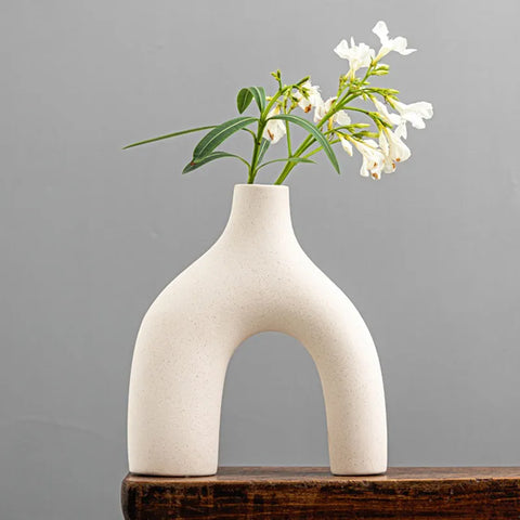 Cream-colored ceramic hiroki vase with unique arch-shaped design holding delicate white flowers